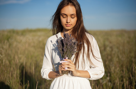Outdoors portrait of a gorgeous young brunette woman holding lavender flowers.の写真素材