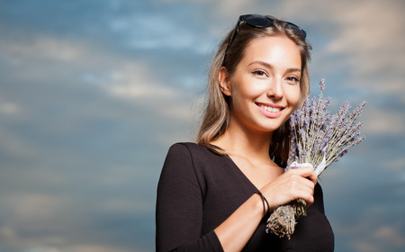 Outdoors portrait of a gorgeous young brunette woman holding lavender flowers.の写真素材