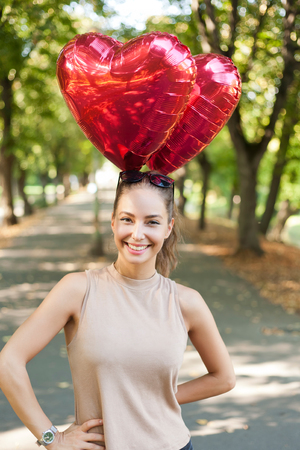 Beautiful cheerful young brunette woman with read heart balloons.の写真素材