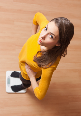 Portrait of a gorgeous young brunette woman standing on a scale.の写真素材