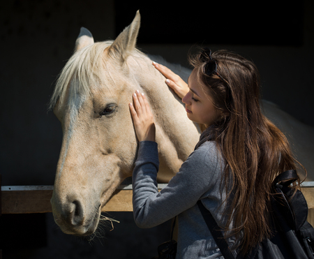 Beautiful young brunette woman befriending champagne color horse.の写真素材
