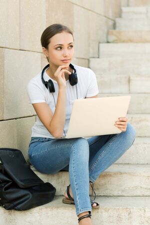 Portrait of attractive young brunette student using her laptop outdoors.の写真素材