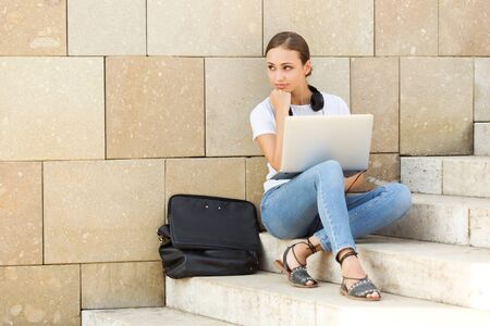 Portrait of attractive young brunette student using her laptop outdoors.の写真素材