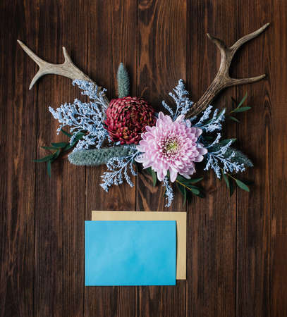 Boho style decor concept. Antlers decorated with flowers near envelopes on rustic wooden background....