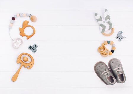 Baby accessories booties, soother and wooden toys on white wooden background with blank space for text. Top view, flat lay.