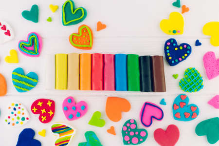 Colorful plasticine neat hearts on white wooden background with blank space for text. Top view, flat...