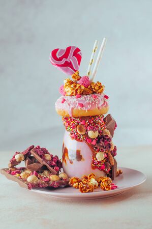 Valentines day raspberry freak shake topping with donut, caramel popcorn and sweets on beige...