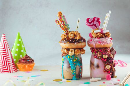 Two freak shakes topping with donut, caramel popcorn and sweets on grey backgroundの写真素材