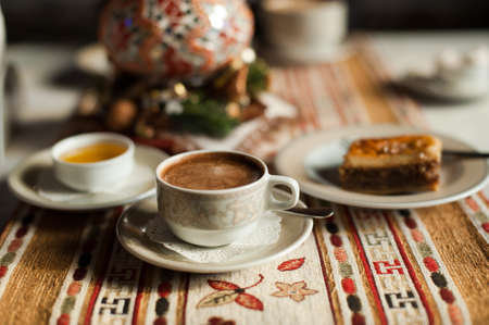 A cup of coffee on the traditional turkish tablecloth with honey and baklava, cup in the focus