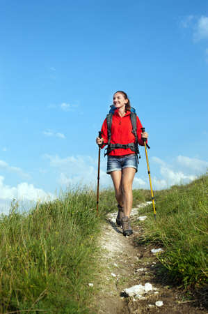 Smiling hiking young woman with backpack and trekking polesの写真素材