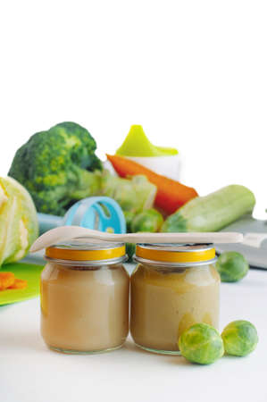 Glass jars with natural baby food on the table: vegetable puree with Brussels sprouts, squash, broccoli, cauliflower, isolated on white background; selective focusの写真素材