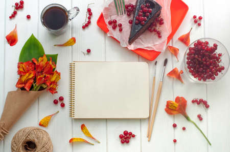 Open empty notebook with cup of coffee, red current cake slice, brushes and bouquet of flowers on the white wooden background, copy space. Top view.の写真素材