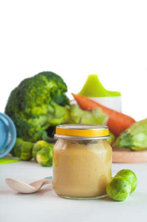 Glass jar with natural baby food on the table, isolated on white background: vegetable puree with Brussels sprouts, squash, broccoli, cauliflower; selective focusの写真素材