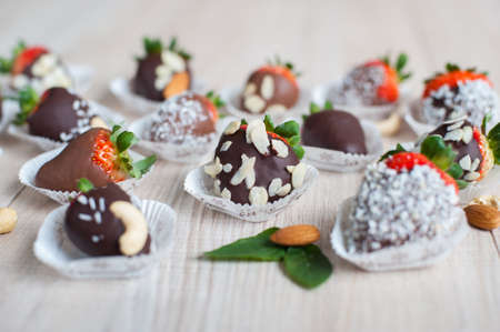 Variety of strawberries covered with milk and dark chocolate and coconut flakes and almond nuts designed as a candy, on the light wooden table; shot in shallow depth of fieldの写真素材