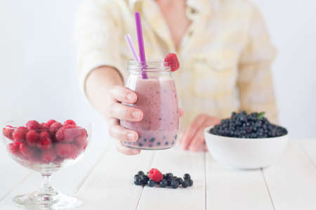 Healthy food concept: close up of a female hand with a smoothie with raspberry and blueberry; selective focus.の写真素材