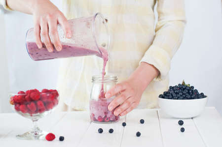 Healthy food concept: close up of a young woman blending apples, berries and bananas to make a smoothieの写真素材
