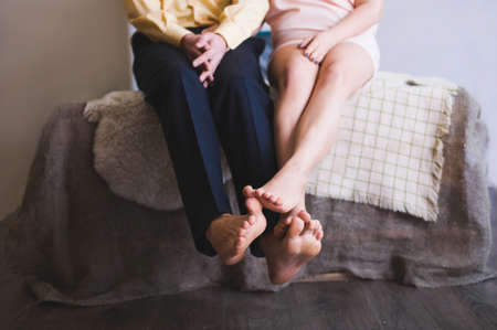 Closeup of feet of young couple in love sitting on sofa, shot in shallow depth of field, fingers in focusの写真素材
