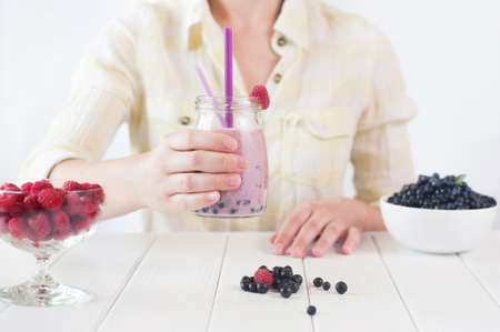 Healthy food concept: close up of a young woman drinking smoothie with raspberry and blueberry; selective focusの写真素材