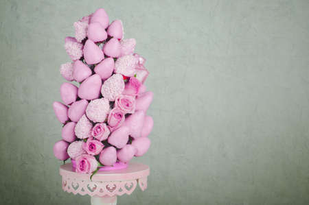 Fresh strawberry covered by pink chocolate with rose flowers designed as a fruit pyramid, gray wall as a backgroundの写真素材