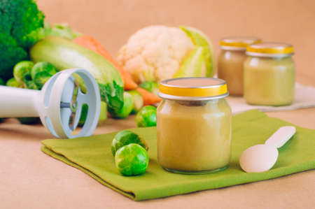 Glass jar with natural baby food on the table: vegetable puree with Brussels sprouts, squash, broccoli, cauliflower; selective focusの写真素材