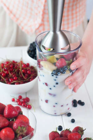 Healthy food concept: close up of a young woman prepare to blending apples, berries and bananas to make a smoothieの写真素材