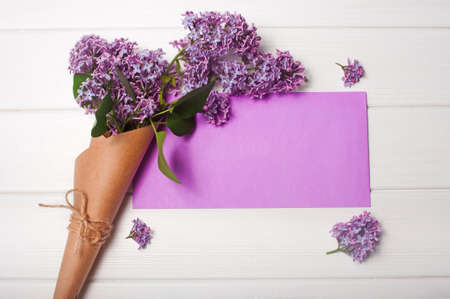 Empty postal envelope and bouquet of lilac flowers on the white wooden background, copy space. Top view.の写真素材