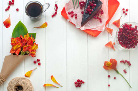 Cup of coffee, red current cake slice and bouquet of flowers in the craft paper on the white wooden background, copy space. Top view.の写真素材