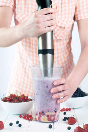Healthy food concept: close up of a young woman blending apples, berries and bananas to make a smoothieの写真素材