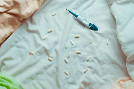 Capsule pills and electronic thermometer on the bedの写真素材