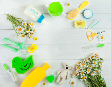 Baby's accessories, toys and chamomile flowers in round shape frame over white wooden background with copy space top view, flat layの写真素材