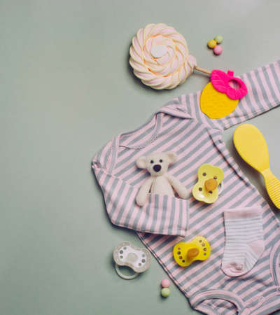 Baby accessories background: baby jumpsuit, socks, soother and toys over gray background with copy...
