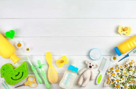 Baby's accessories near chamomile flowers over white wooden background with copy space top view,...