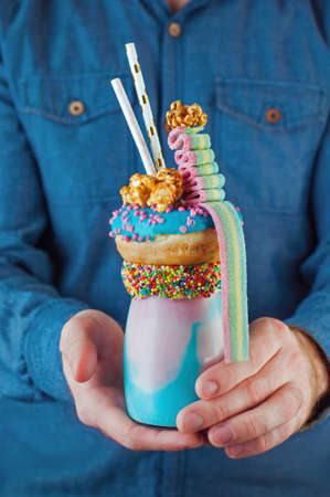 Males hands holding freak shake topping with donut, popcorn and marmalade over pink background with...