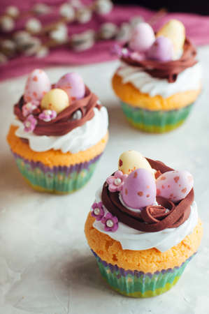 Happy Easter card: Easter vanilla cupcakes decorated with candy eggs in nest on gray background selective focusの写真素材