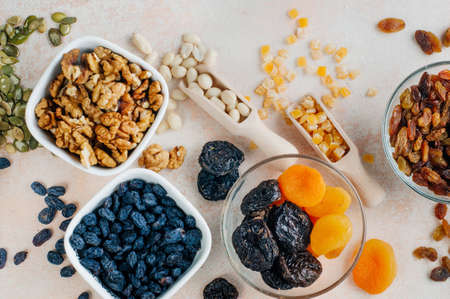 Close up of dried fruits, nuts and seeds in ceramic and glass bowls on light beige background top view, flat layの写真素材