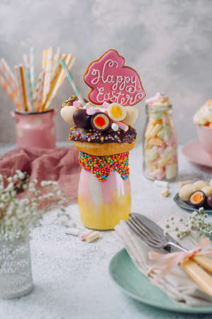Easter freak shake decorated with Easter bunny gingerbread topping with donut, chocolate eggs and marshmallow on the decorated table selective focusの写真素材