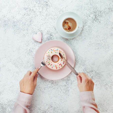 Breakfast concept: Close up of female hands with fork and knife cutting donut shape biscuit on gray stone background top view, flat layの写真素材