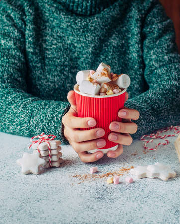 Female hands holding coffee cup with marshmallow and star shaped cookies on gray background selective focusの写真素材