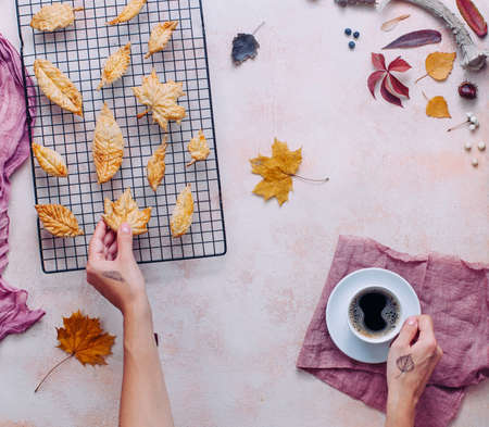 Female hands with cup of coffee and leaves shaped cookies on beige stone background top view, flat layの写真素材