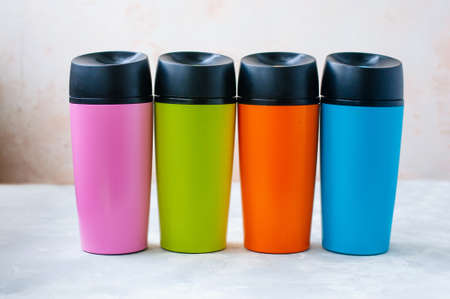 Four plastic color thermal mugs on gray background selective focus