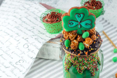 St. Patrick's Day party table: Green freak shake topping with clover and rainbow cookies, donut, caramel popcorn and chocolate cupcakes on gray background selective focus, copy spaceの写真素材