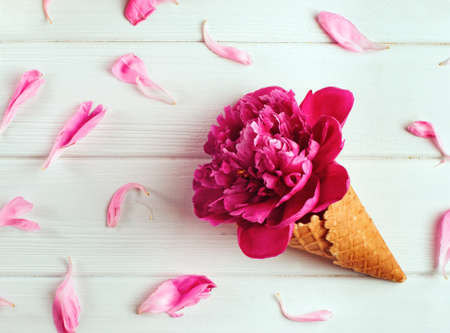 Spring floral background: Ice cream waffle cone with peony flowers on the white wooden background. Top view, flat layの写真素材