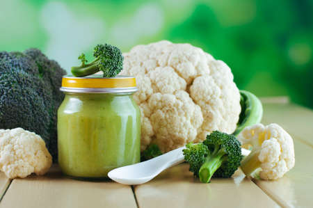 Natural baby food on the wooden background: jars with vegetable broccoli and cauliflower puree with spoon selective focusの写真素材