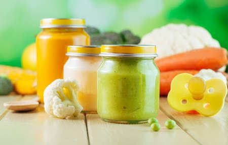 Natural baby food concept: jars with vegetable puree on the light wooden background broccoli, cauliflower, potato, carrot, green pea selective focusの写真素材