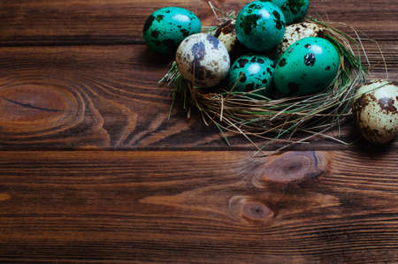 Easter decoration concept: Painted quail eggs in natural nest over rustic wooden background with copy space selective focusの写真素材