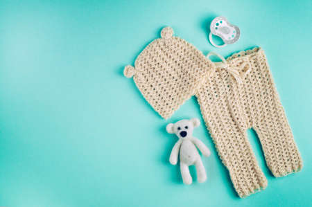 Baby accessories background: small hat and pants for newborn baby, dummy and bear toy on blue background with copy space top view, flat layの写真素材