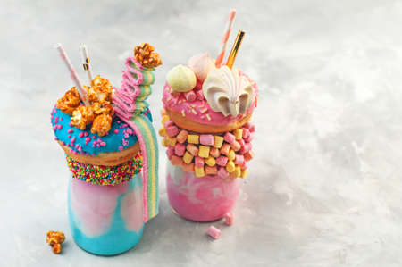 Two color freak shakes topping with donut, marshmallow, meringues, popcorn and marmalade over gray...