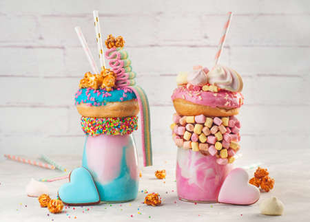Happy Birthday party background: Two freak shakes topping with donut, marshmallow, popcorn and marmalade near heart biscuits selective focus.の写真素材