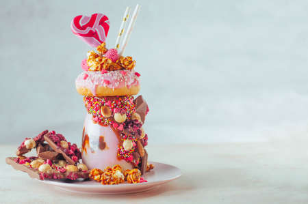 Raspberry freak shake topping with donut, popcorn and sweets on gray background with copy space; selective focus.の写真素材