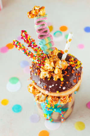 Kids party concept: Top view of chocolate freak shake topping with donut and caramel popcorn on the party table; selective focus.の写真素材